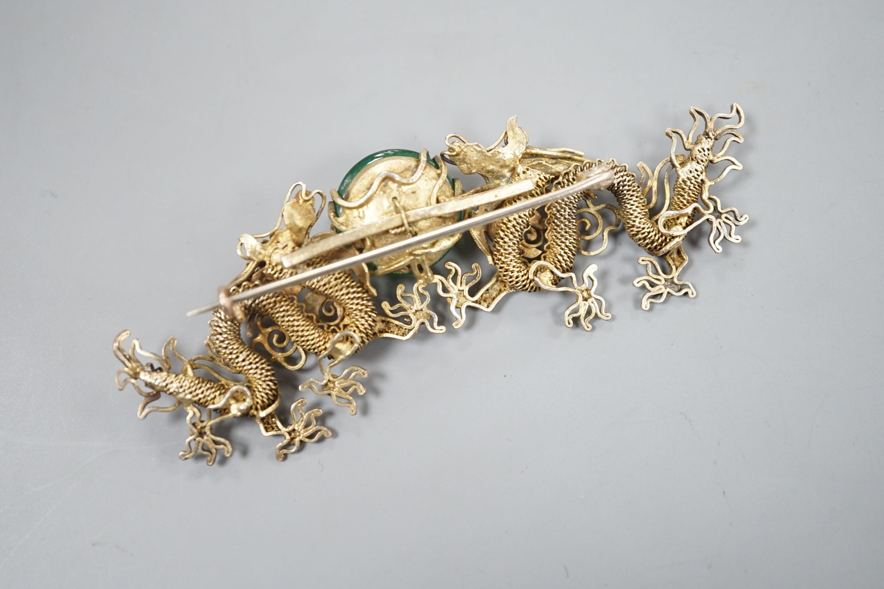 A Chinese gilt white metal and green cabochon stone set filigree dragon brooch, 88mm.